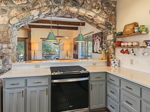 Una cocina con arco de piedra, estufa empotrada y un ventanal grande.