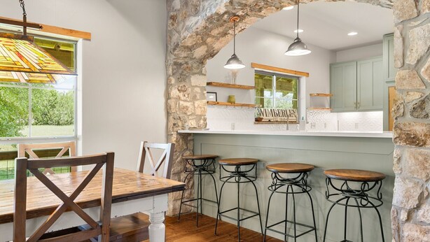A rustic kitchen with a stone archway, wooden bar stools, and a wooden dining table.