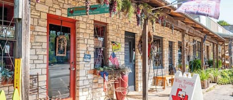Un bâtiment rustique avec une façade en pierre, une porte rouge et une enseigne indiquant qu’il propose des dégustations de vin et vend des cadeaux.