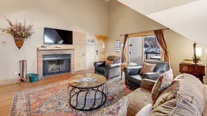 A spacious living room with a fireplace, leather sofas, a flat-screen TV, and a large window offering a view. - Downtown Location - Steps to Gondola, Hot Tub, DOG FRIENDLY SCC3 (Breckenridge)