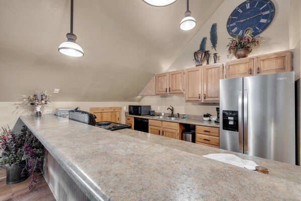 A kitchen with granite countertops, stainless steel appliances, wooden cabinets, and pendant lighting.