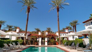 A pool area with lounge chairs, palm trees, and a building with a tiled roof.