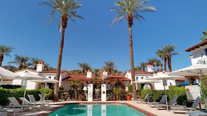 A pool area with lounge chairs, palm trees, and a building with a tiled roof.