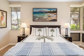 A bedroom with a bed, two nightstands, a painting of a beach, and a window with blinds.