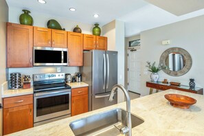 A modern kitchen with wooden cabinets, stainless steel appliances, and a marble countertop.