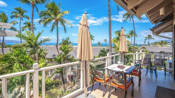 Un balcon avec une table et des chaises, donnant sur un paysage tropical avec des palmiers et une vue sur l’océan.