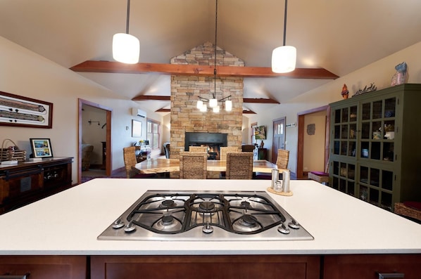 A kitchen with a central island, a stone fireplace, and hanging pendant lights.