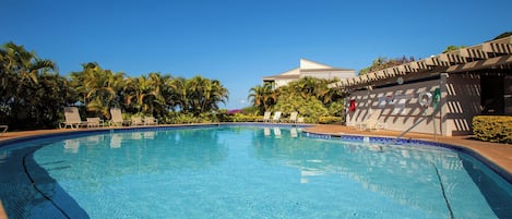 Una piscina azul cristalina con sillas de descanso y palmeras.