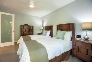 A hotel room with two beds, a wooden headboard, bedside tables with lamps, and a door with frosted glass.