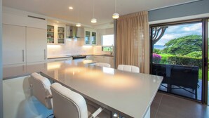 Een moderne keuken met een centraal eiland, witte kasten en uitzicht op groen via een schuifdeur.