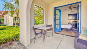 A patio with a table and chairs, a blue door leading to a bedroom, and a view of a garden.