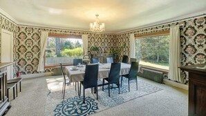 A dining area with a table set for four, a chandelier, patterned wallpaper, and large windows with curtains. - Antique, HOT TUB, Game Room, Theater, Dogs Ok (Bloom) (Seaview)