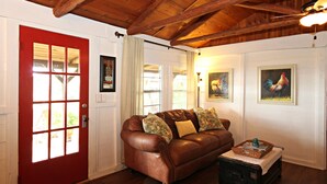 A living room with a brown leather sofa, a red door, and wooden beams on the ceiling.