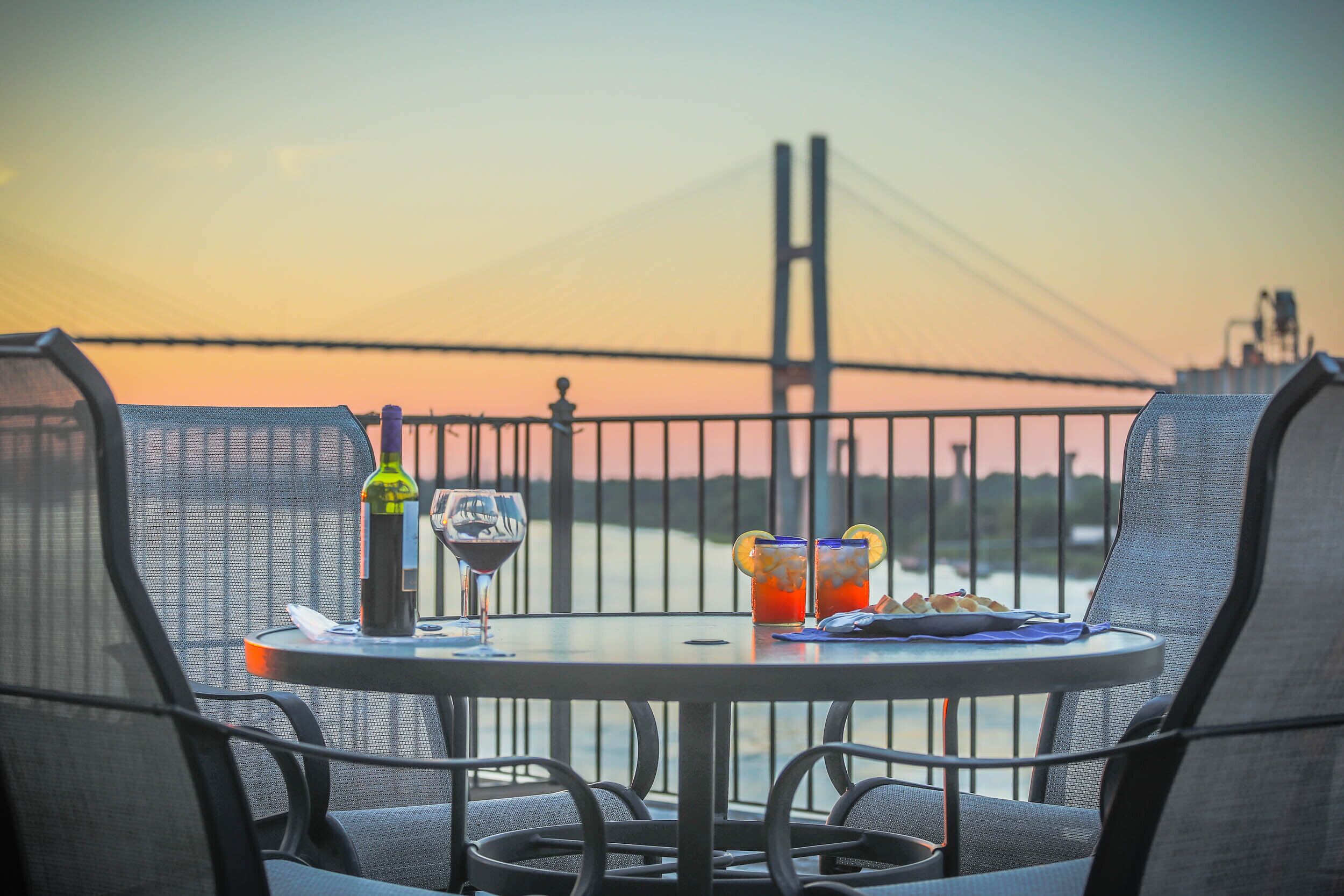A table with drinks and a bottle, overlooking a bridge and water.