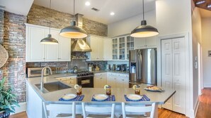 A modern kitchen with white cabinets, a large island with bar stools, and pendant lighting.