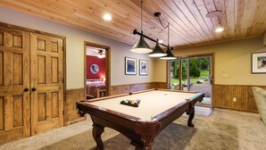 Een pooltafel in een ruimte met houten wanden en plafond, een deur en een raam.