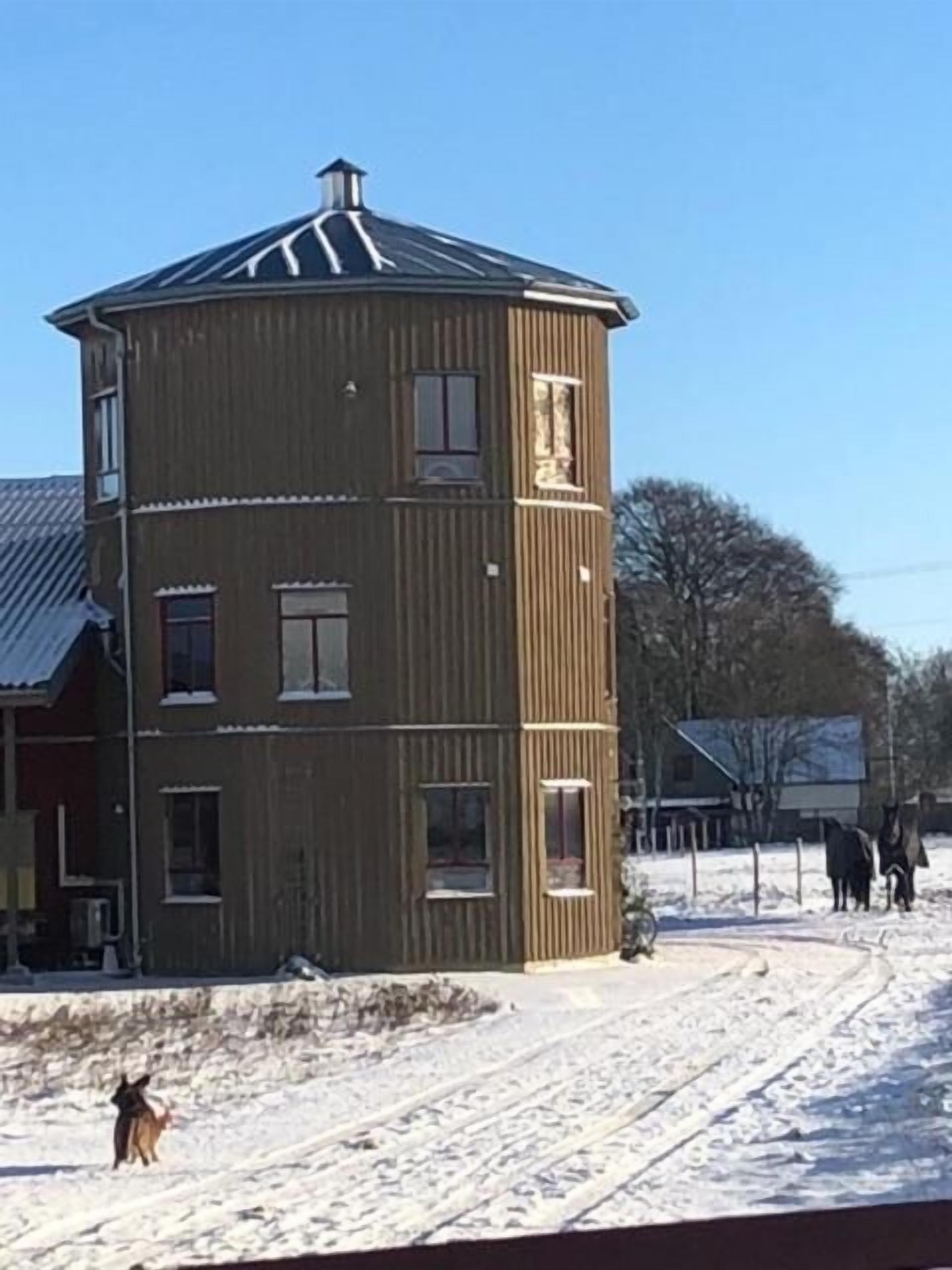 Een meerlaags houten gebouw met een schuin dak, omringd door een besneeerd landschap en enkele paarden.