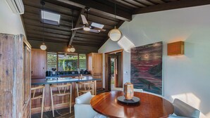 A modern kitchen with wooden cabinets, a central island, and pendant lighting. - Luxurious Beachfront Retreat (Hanalei)