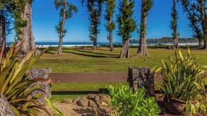 A grassy area with tall trees and a wooden fence, overlooking a body of water. - Luxurious Beachfront Retreat (Hanalei)