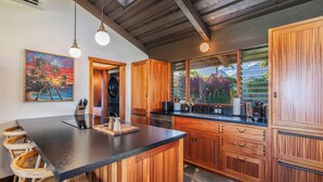 A kitchen with a large island, wooden cabinets, and a painting of a sunset. - Luxurious Beachfront Retreat (Hanalei)