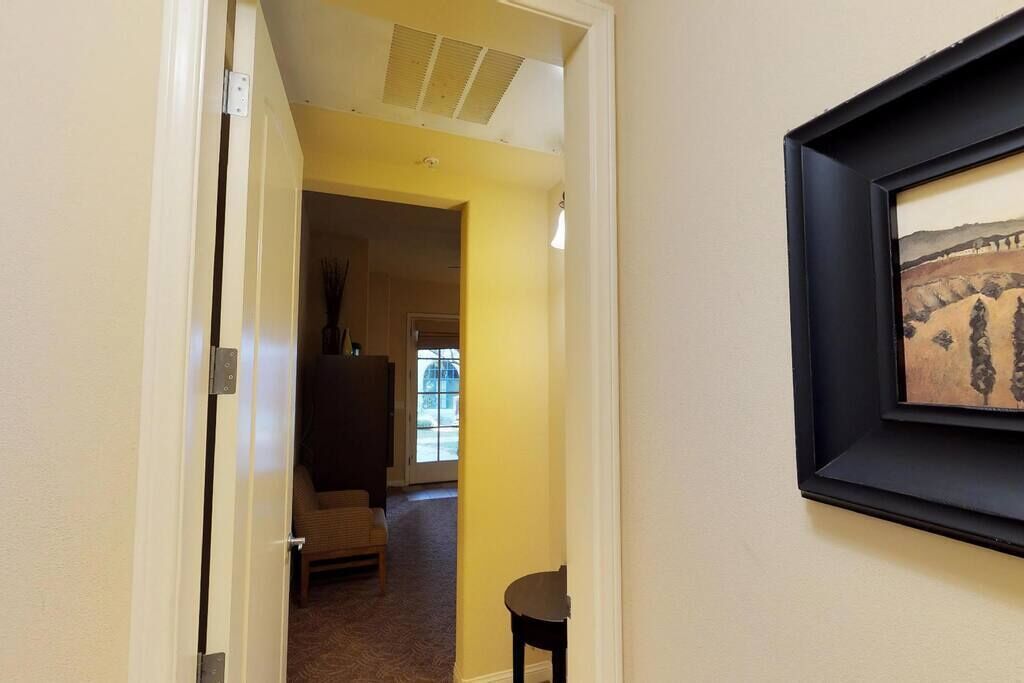 A hallway with a door leading to a room, a framed picture on the wall, and a small table.