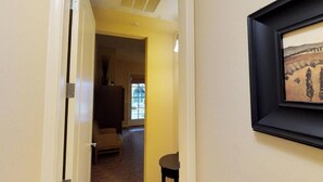 Un couloir avec une porte donnant sur une pièce, un tableau encadré accroché au mur et une petite table.