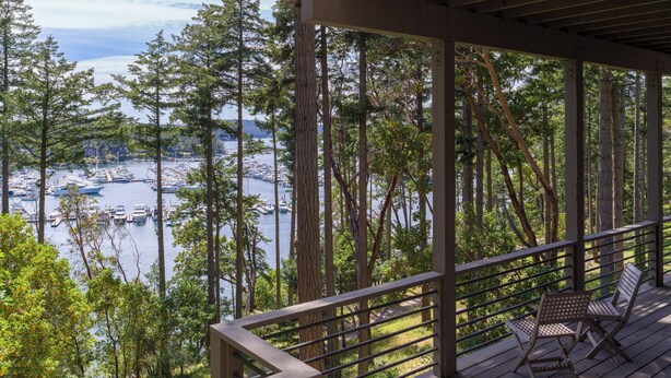 A wooden deck with a railing overlooking a marina with boats and tall trees. - San Juan Island, Roche Harbor Overlook #196 (Roche Harbor)