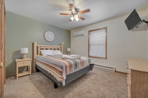 A bedroom with a bed, bedside tables, a ceiling fan, a wall-mounted TV, and a window with blinds.