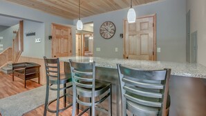 A kitchen with a wooden ceiling, a large island with bar stools, and a wall clock.