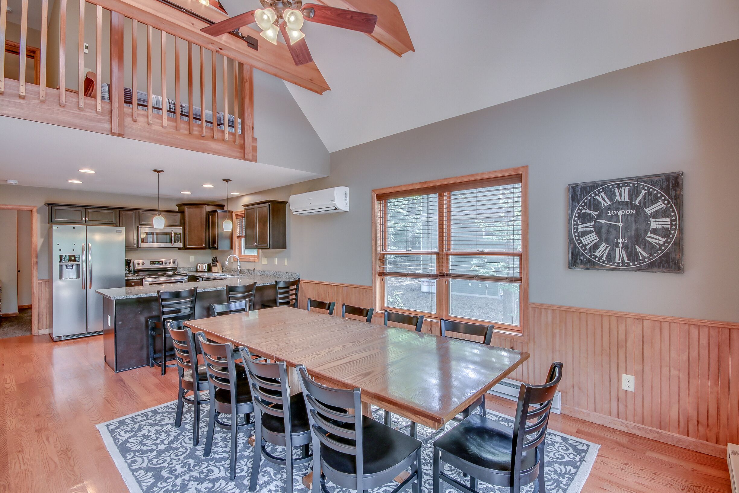 A spacious kitchen with modern appliances, a dining area with a wooden table and chairs, and a large clock on the wall.