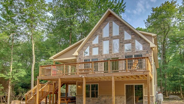 A two-story cabin with a balcony, wooden deck, and stone exterior.