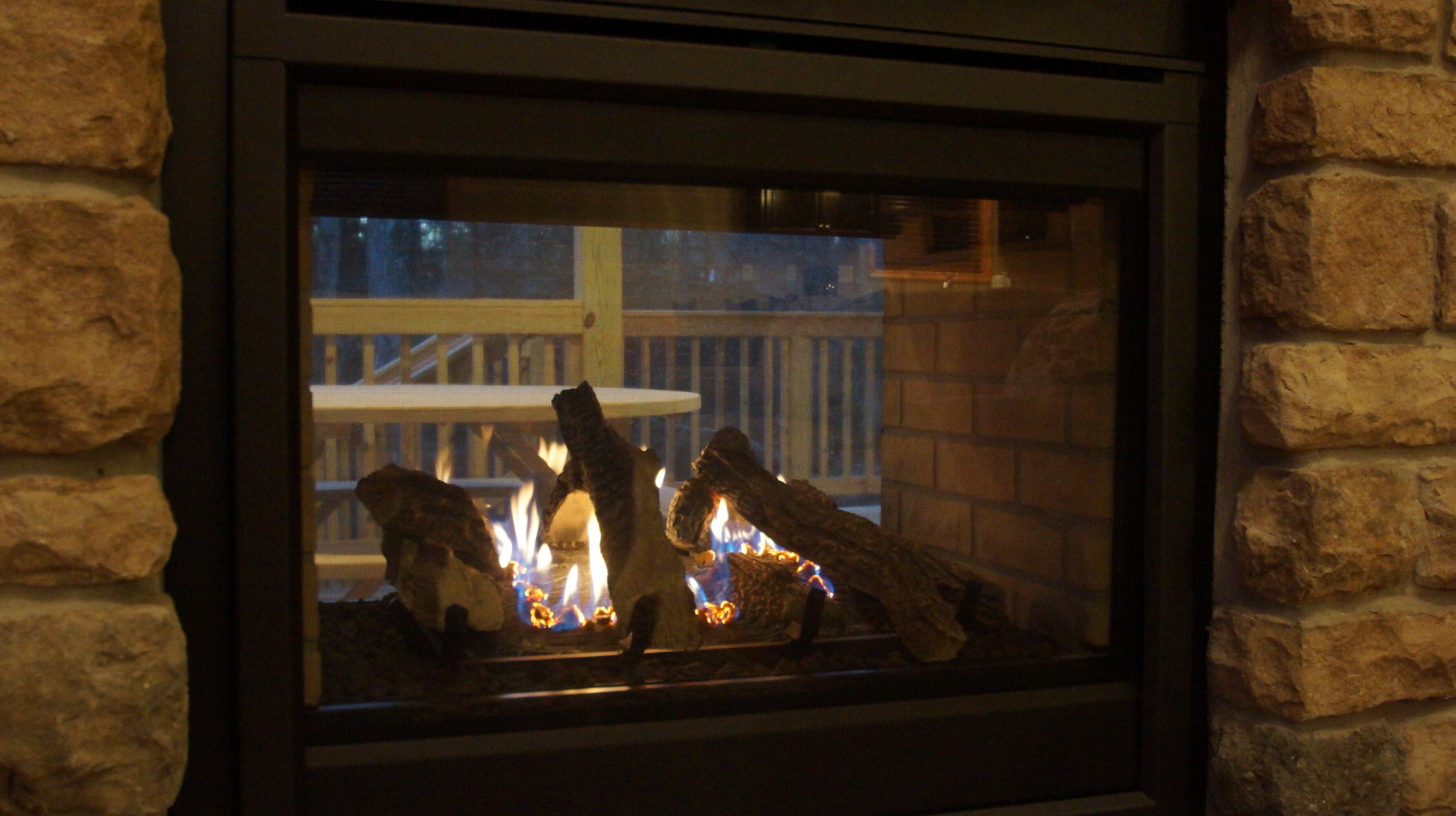 A fireplace with logs and flames, set in a stone wall.