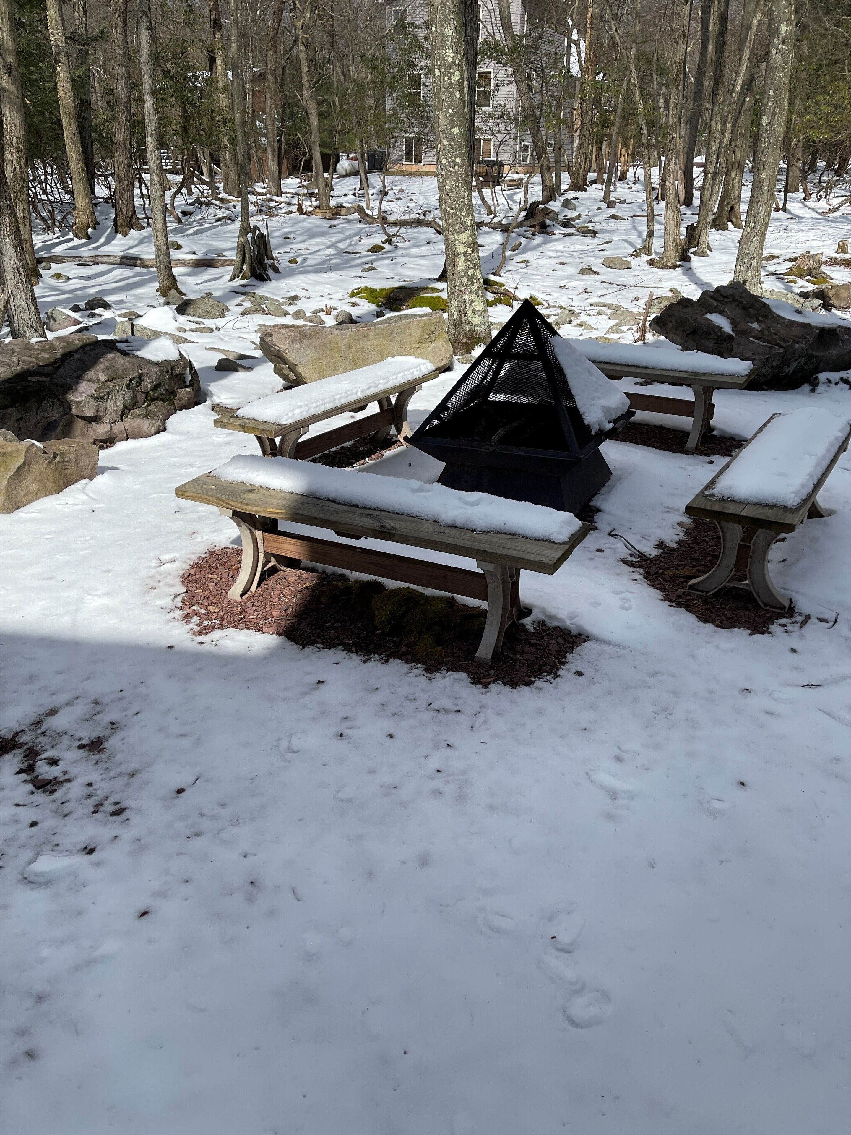 A snow-covered outdoor area with picnic tables and a fire pit.
