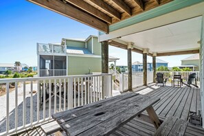 A wooden deck with a covered seating area, white railings, and a view of a beach and buildings in the background. - Sea Turtle | 6BR/5.5BA Fort Morgan Beach Home | Sleeps 17 | Gulf & Bay Views (Gulf Shores)