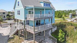 Ein zweigeschossiges Strandhaus mit Balkon, Holzterrasse und einer kleinen Treppe, die zum oberen Geschoss führt.