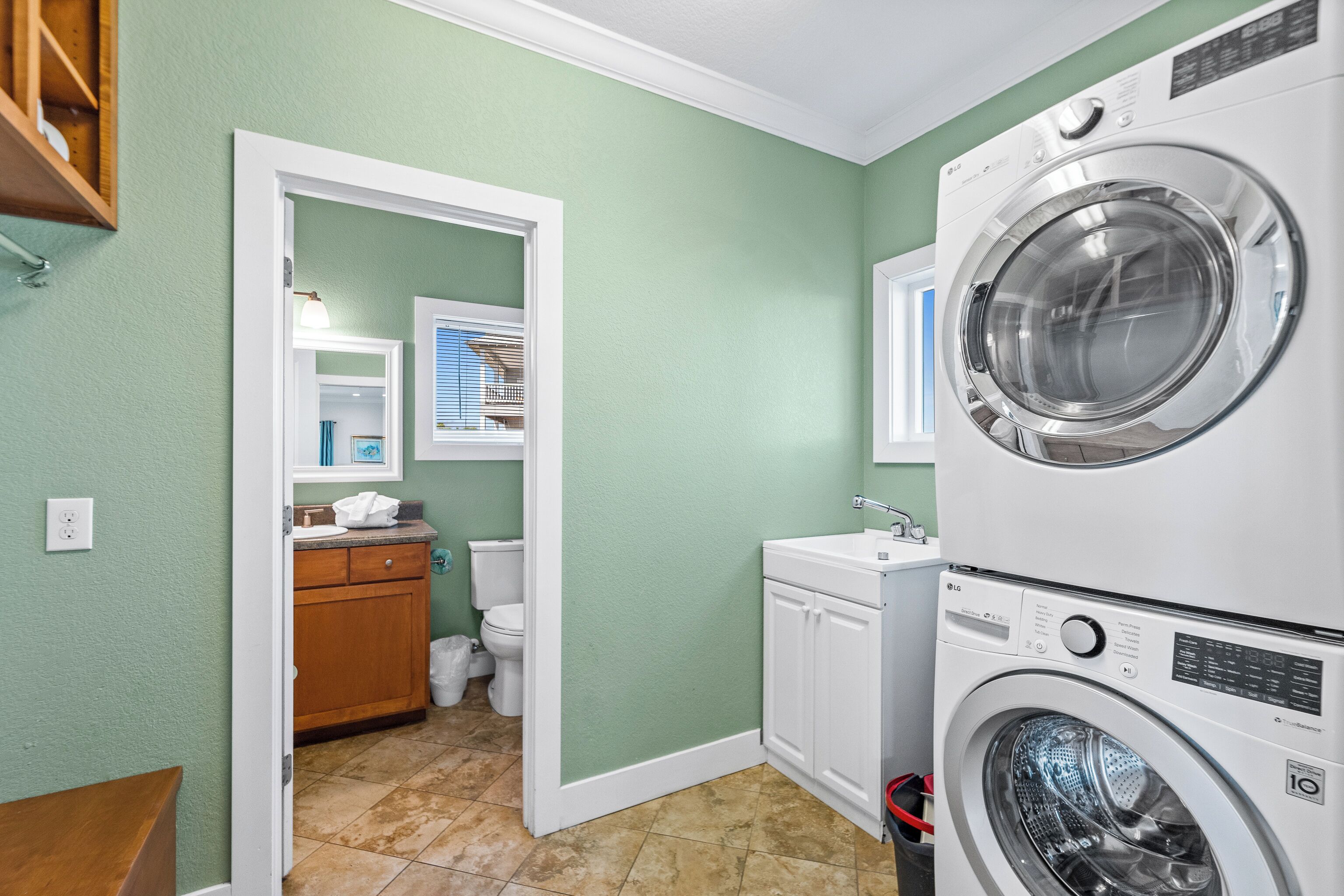 A laundry room with a stacked washer and dryer, a wooden cabinet, and a white sink.