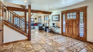 A spacious hallway with a wooden staircase, a seating area with a sofa and coffee table, and a large wooden door with glass panels. - Free SkyCard - Spacious Luxury Home, Private Hot Tub, Theater - Casa de Plata (Breckenridge)