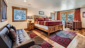 A bedroom with a wooden bed, a leather sofa, a patterned rug, and large windows with curtains. - Free SkyCard - Spacious Luxury Home, Private Hot Tub, Theater - Casa de Plata (Breckenridge)