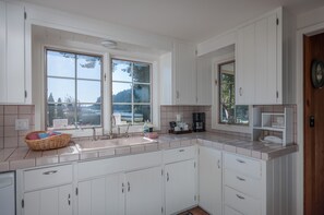 A kitchen with white cabinets, a large window, and a view of the outdoors. - Orcas Island, Marina View #201 (Eastsound)