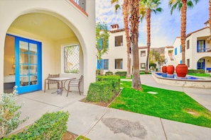 A courtyard with a table and chairs, a blue door, and a pool with red planters. - LV018 Downstairs Legacy Villa Studio by Clubhouse (La Quinta)