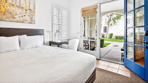 Un dormitorio con una cama grande, un escritorio y una silla. Hay una puerta corrediza de vidrio que da a un espacio exterior con una mesa y sillas.