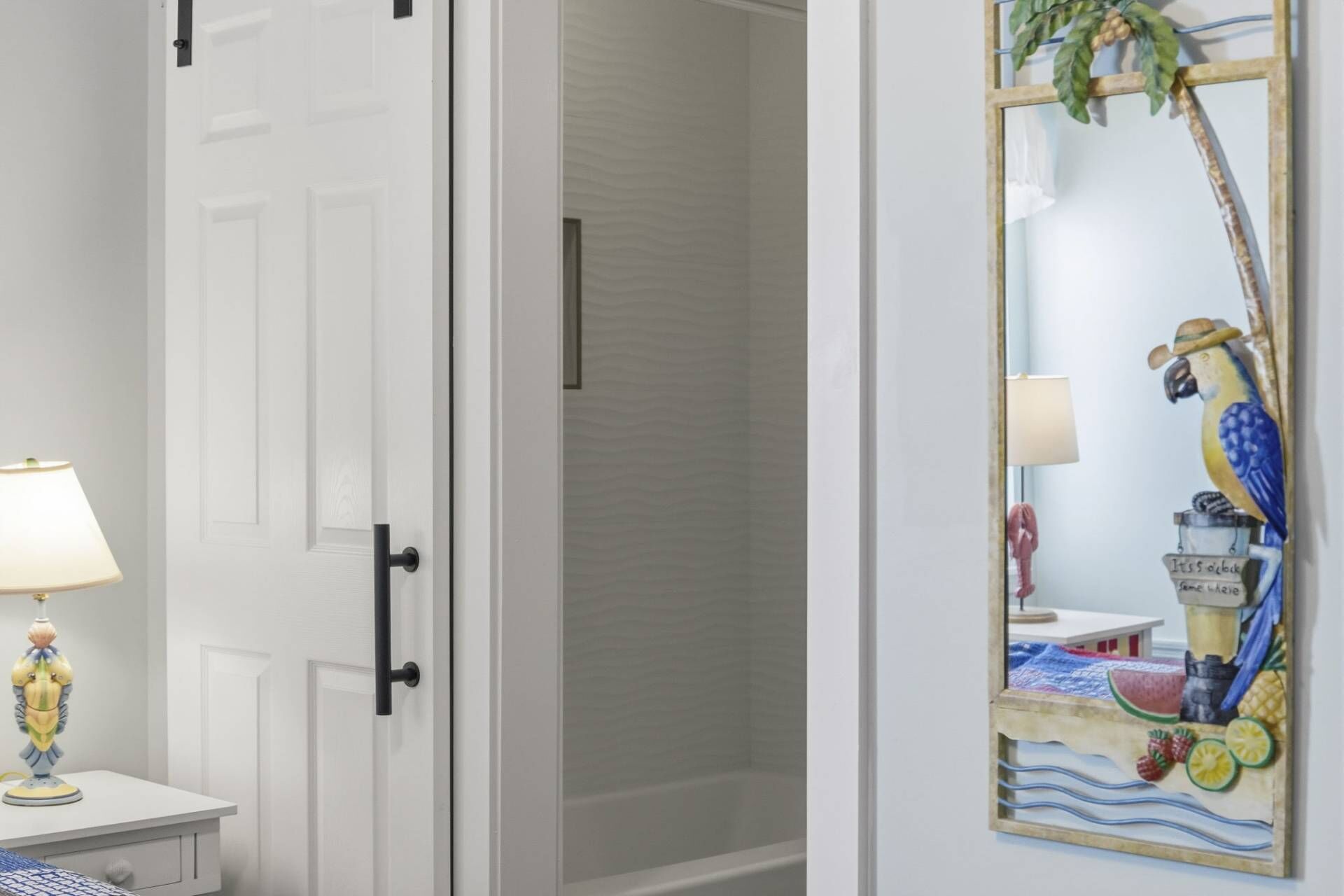 A room with a white door, a small table with a lamp, and a mirror with a tropical design.