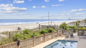 Une vue sur la plage avec une piscine, des chaises longues et un poste de surveillance pour les sauveteurs.