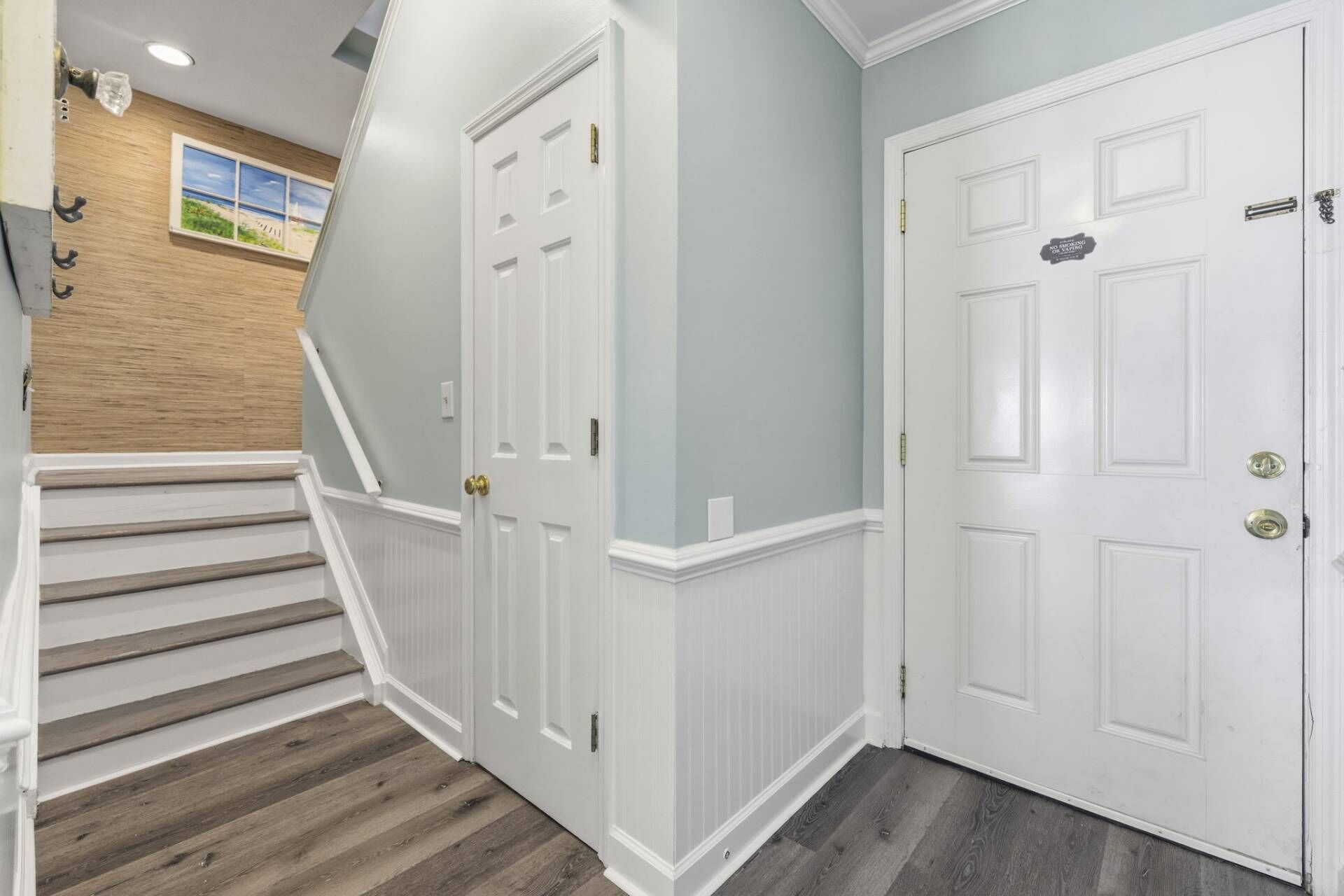 A hallway with white doors, a wooden staircase, and a light blue wall.