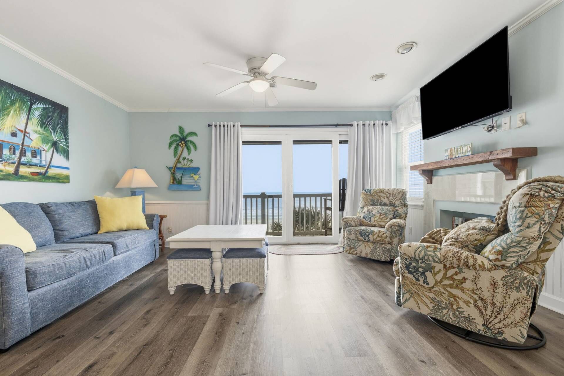 A living room with a sofa, armchairs, a TV, a ceiling fan, and a view to the outside.
