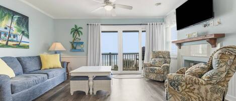 A living room with a sofa, armchairs, a TV, a ceiling fan, and a view to the outside.