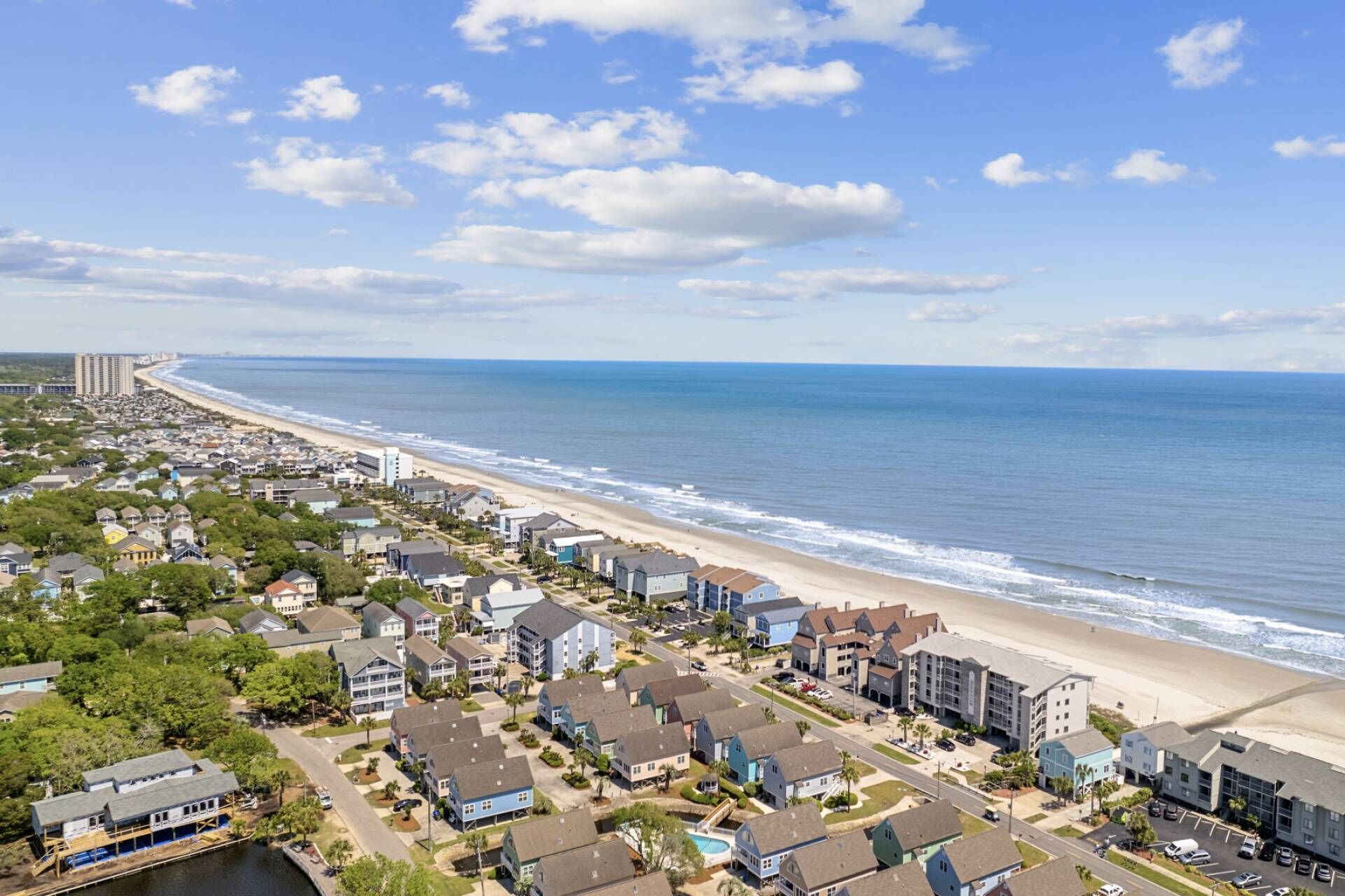 Un quartier résidentiel situé sur la côte, avec des maisons le long de la plage, un ciel dégagé et une vue sur l’océan.