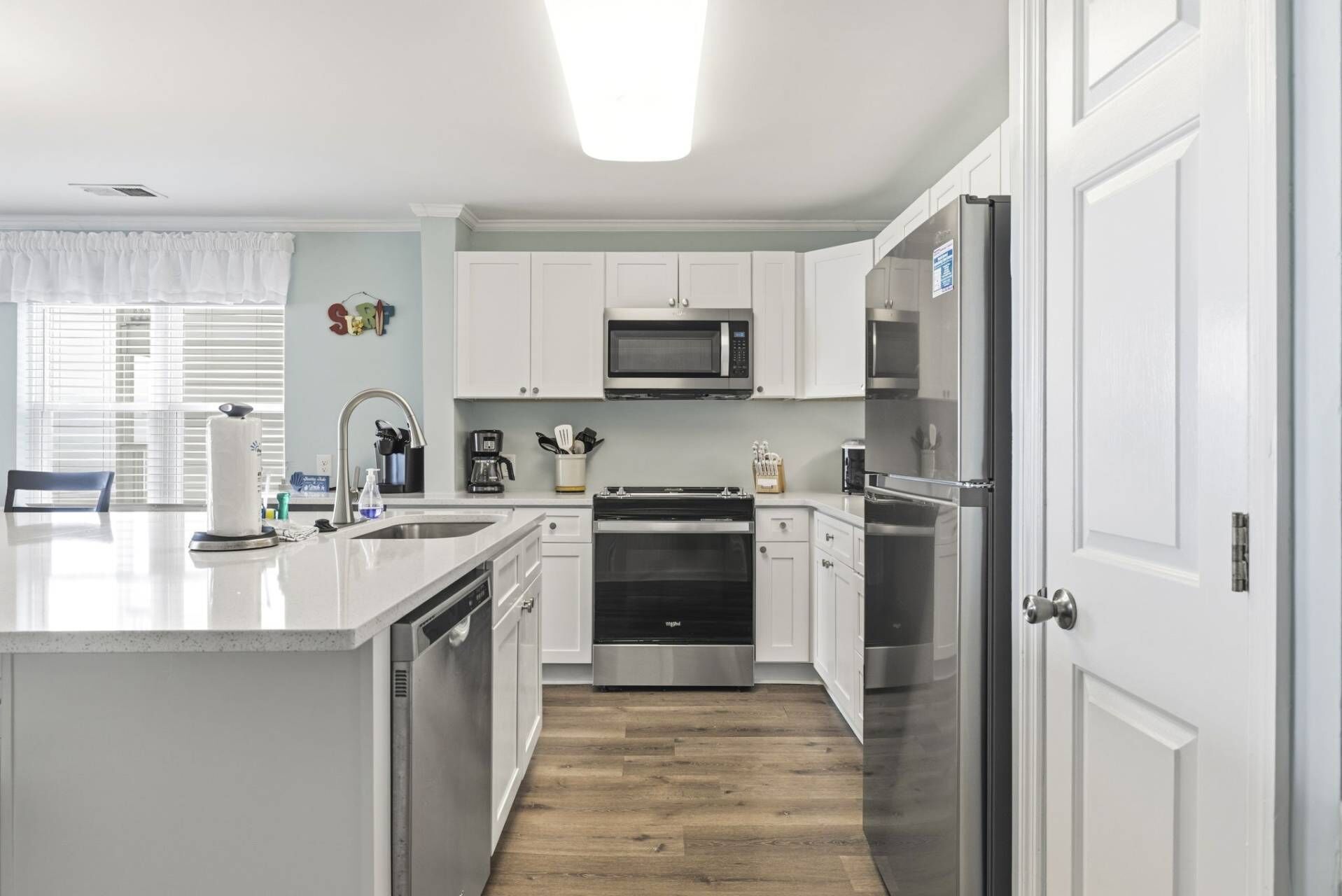 A modern kitchen with white cabinetry, stainless steel appliances, and a wooden floor.