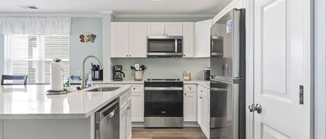 A modern kitchen with white cabinetry, stainless steel appliances, and a wooden floor.