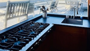 A kitchen with a gas stove, a hanging pot rack, and a view of the beach. - Classic Oceanfront Stinson - The Whale House (Stinson Beach)